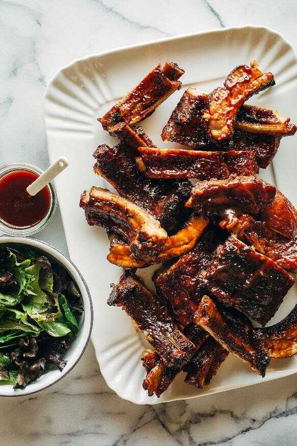 Seasoned grilled ribs with barbecue sauce served on a tray with a bowl of salad and sauce.