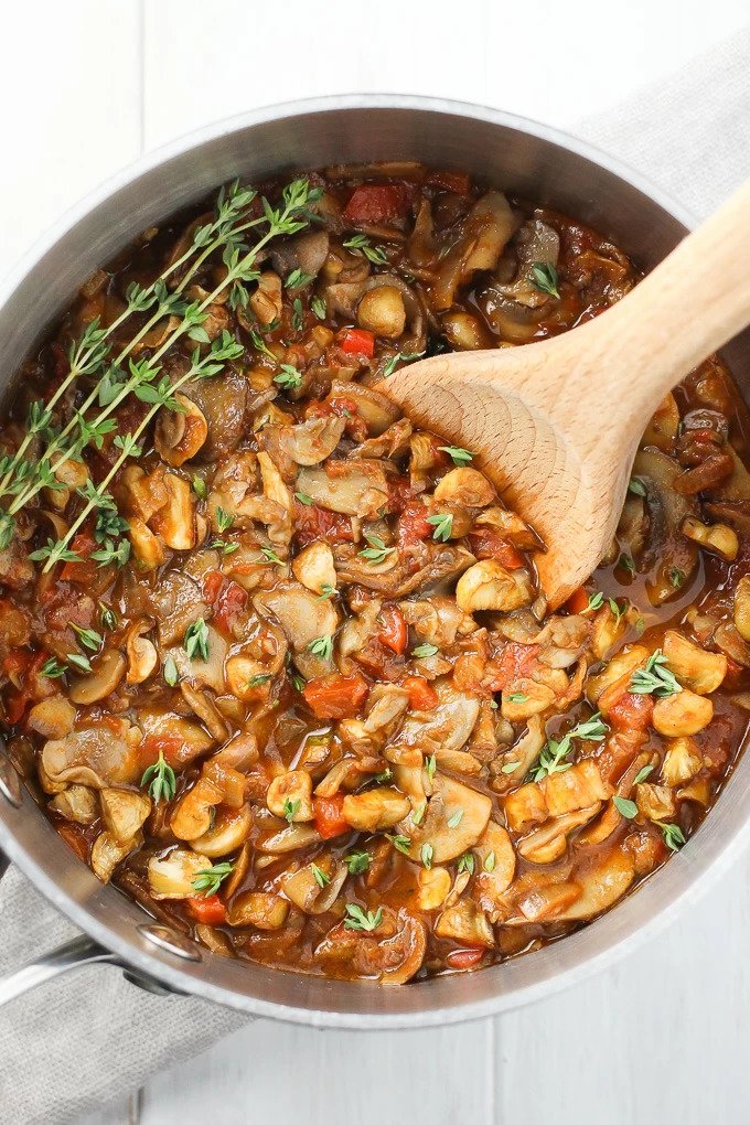 Mushroom and vegetable stew in a pot with a wooden spoon.