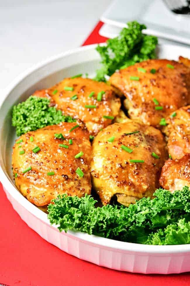 Křupavá kuřecí stehna ochucená kurkumou v pikantní omáčce, obložená listovou zeleninou a servírovaná na talíři.