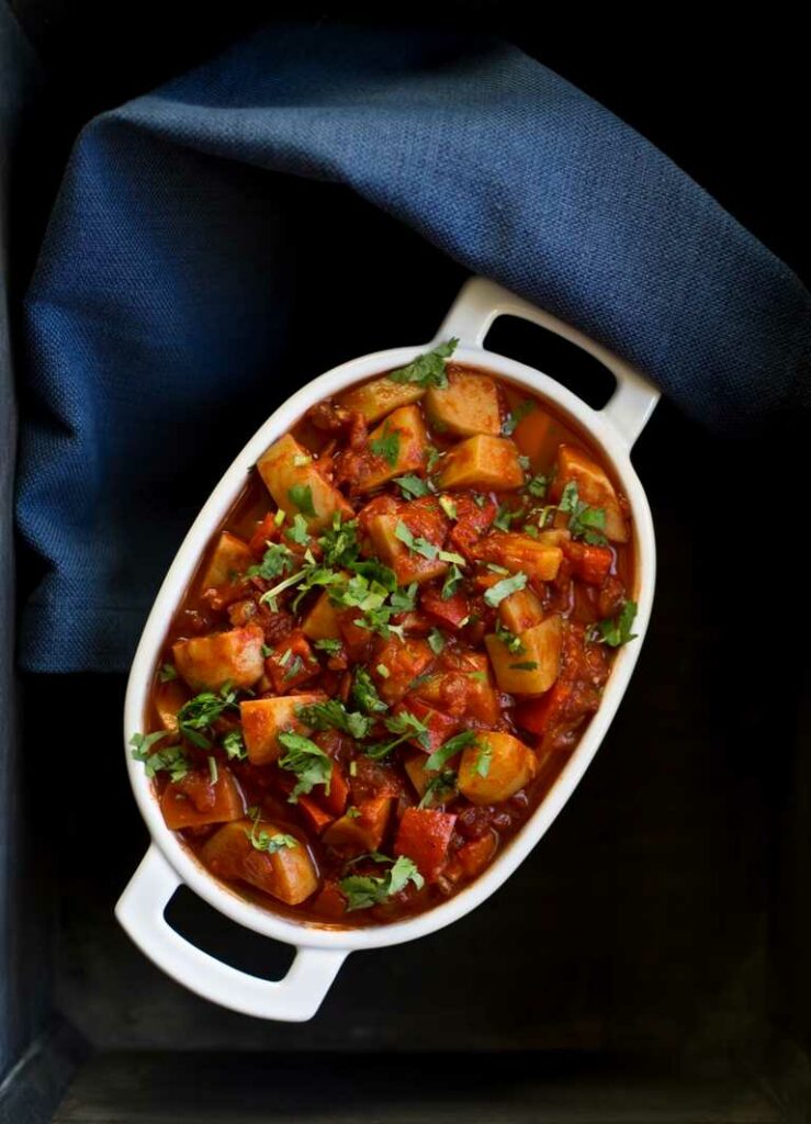 Potato and red pepper stew served in a large bowl and sprinkled with fresh herbs.