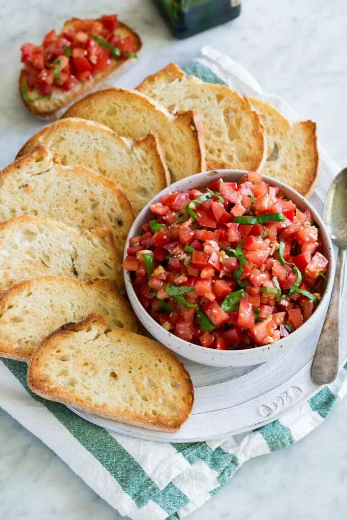 Tomatenmischung mit Basilikum in einer Schüssel, bedeckt mit gerösteten Brotscheiben, alles auf einem Teller serviert.