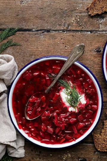Beetroot soup served in a deep plate with a spoon, garnished with sour cream and dill.