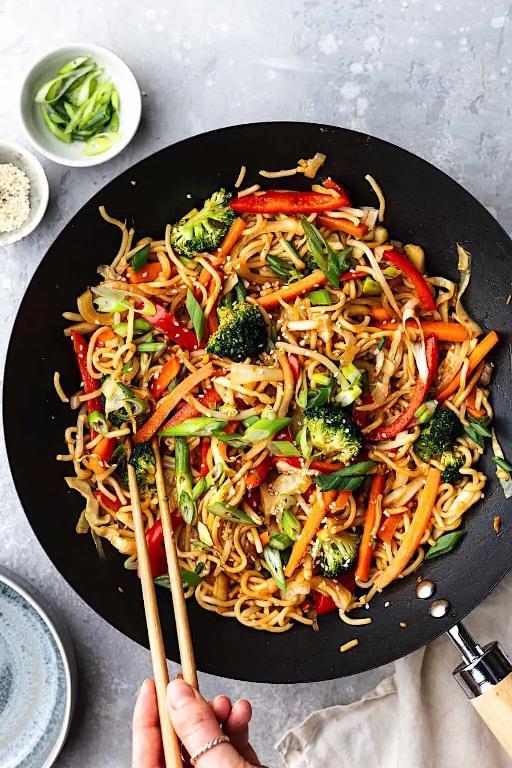 Chinese noodles with vegetables and spicy sauce in a pan, scooped up with chopsticks.