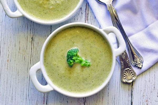 Broccoli soup served in bowls and garnished with broccoli florets.