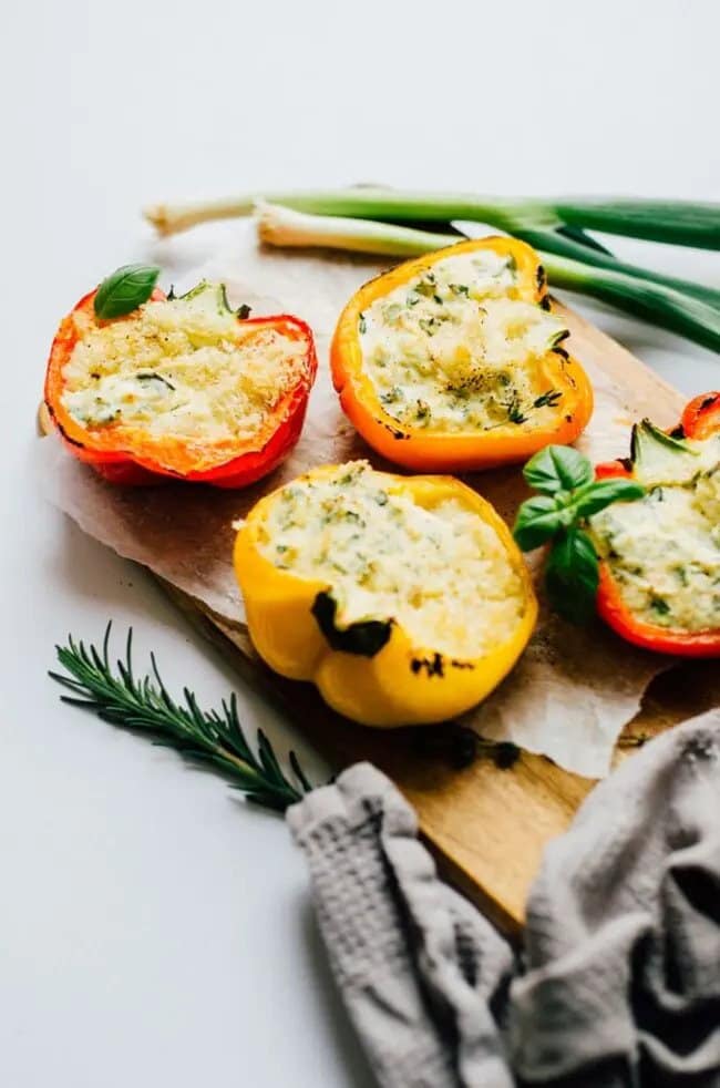 Peppers stuffed with fresh herbs, creamy ricotta and bold parmesan cheese, served on a wooden board with spring onions on the side.