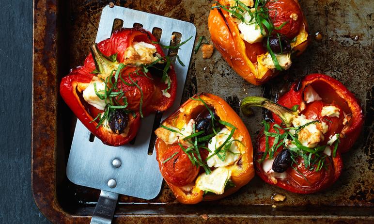 Halves of peppers stuffed with cheese, tomatoes and olives on a baking sheet.