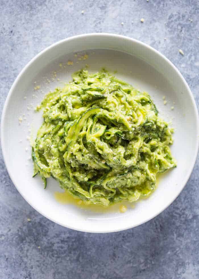 Zucchini spirals covered in a creamy avocado-herb sauce served on a plate.