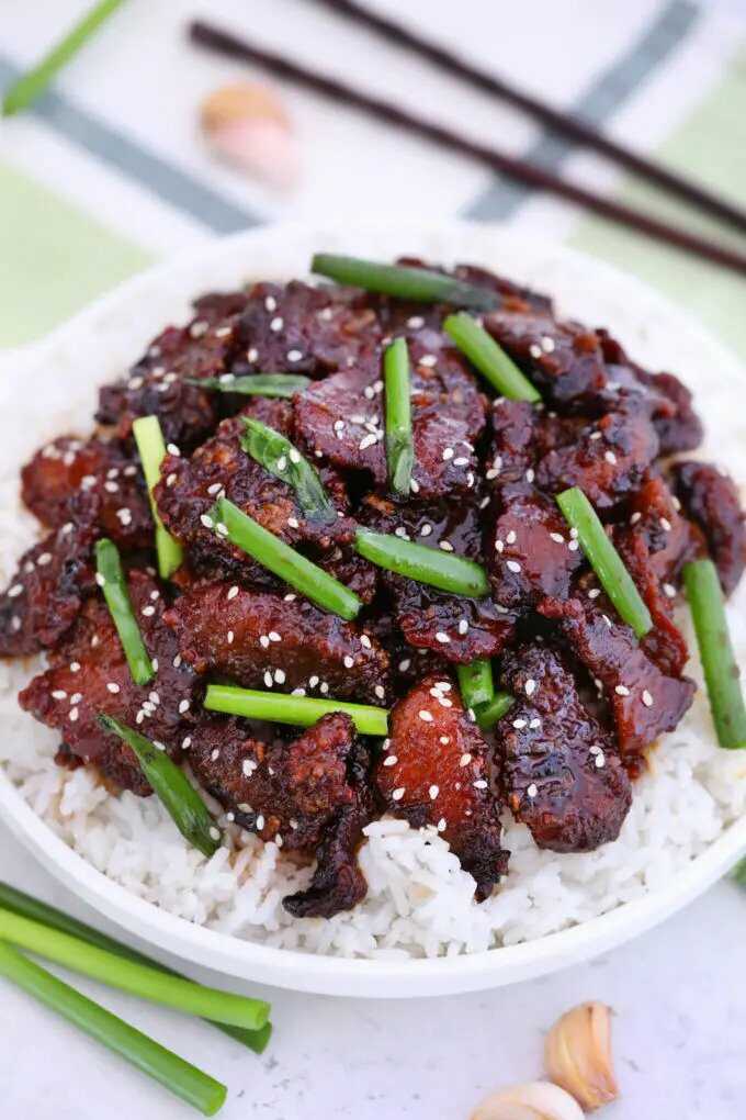 Hovězí maso po mongolsku s jarní cibulkou, servírované v hlubokém talíři s rýží.