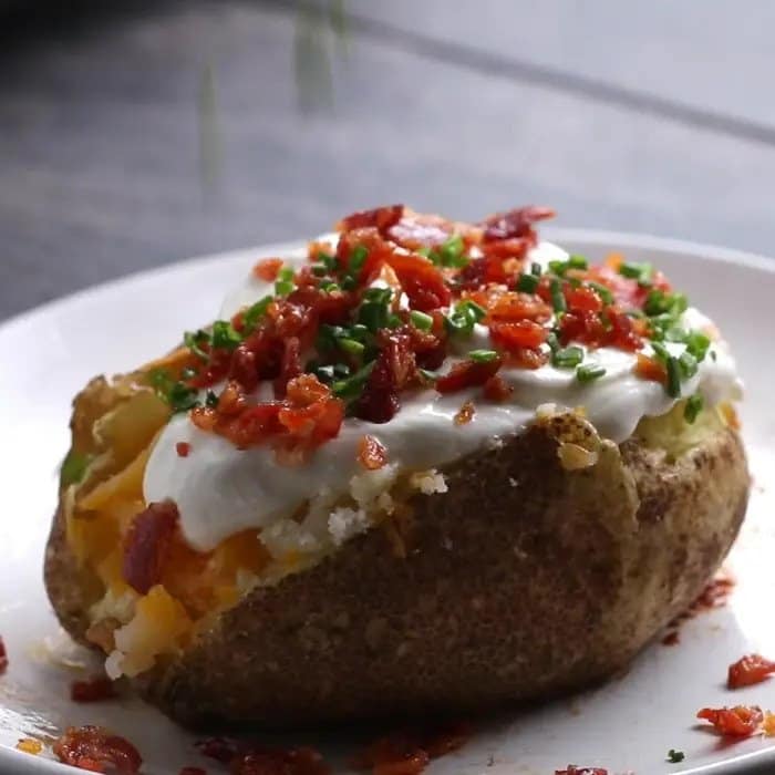 Potatoes with cheese, decorated with bacon, sour cream and chives, served on a plate.