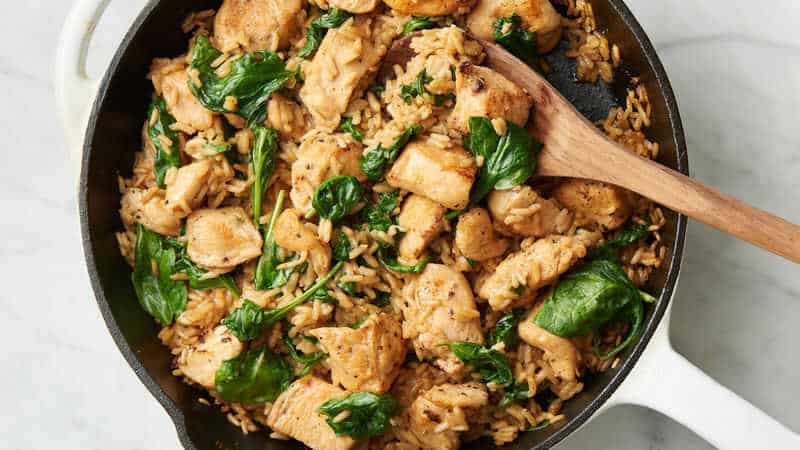 Rice, meat and spinach in one pan with a wooden spoon.