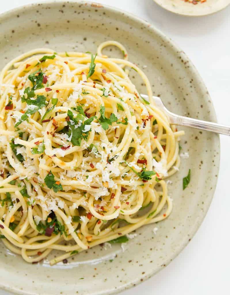 Špagety posypané sýrem a petrželkou servírované v hlubokém talíři s vidličkou.