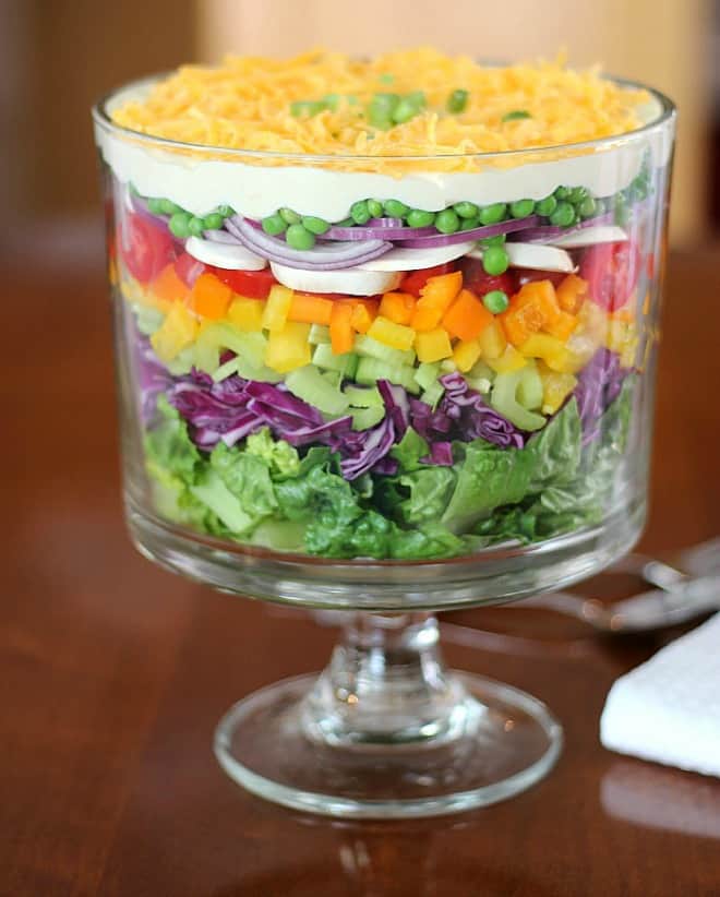 Layers of vegetables served on top of each other in a salad bowl, topped with cheese and spring onions.