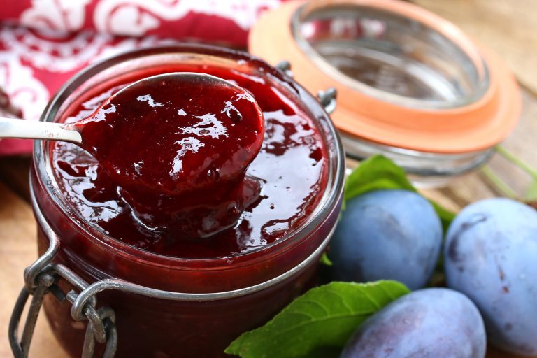 Plum jam in a jar with fresh plums next to it.