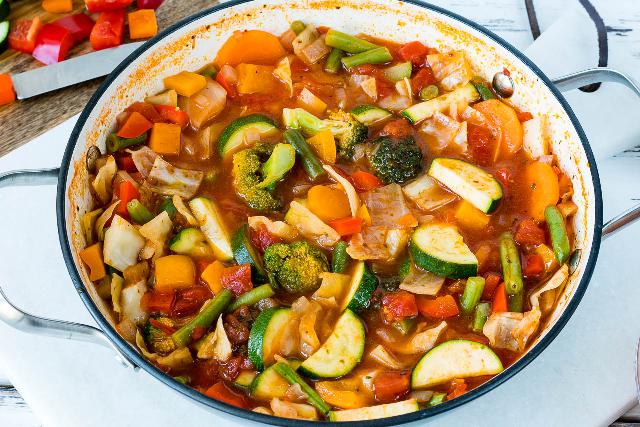 Broccoli, tomato, carrot, pepper, cabbage and zucchini soup served in a deep pan.