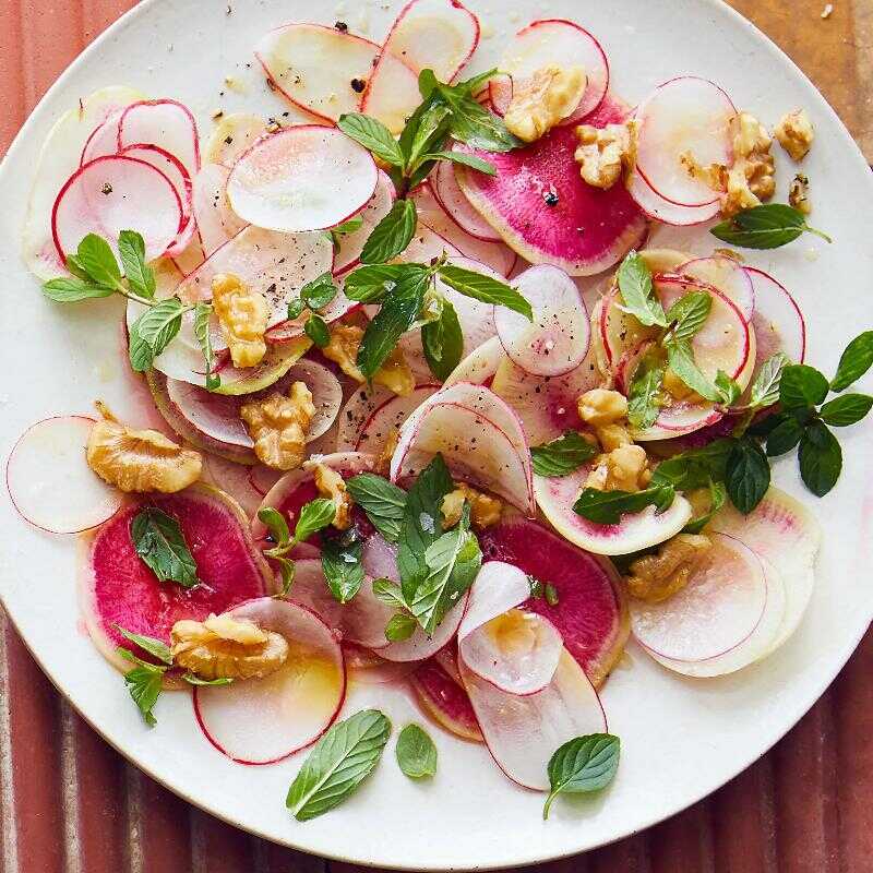Radish slices with lemon dressing, walnuts and mint served on a plate.