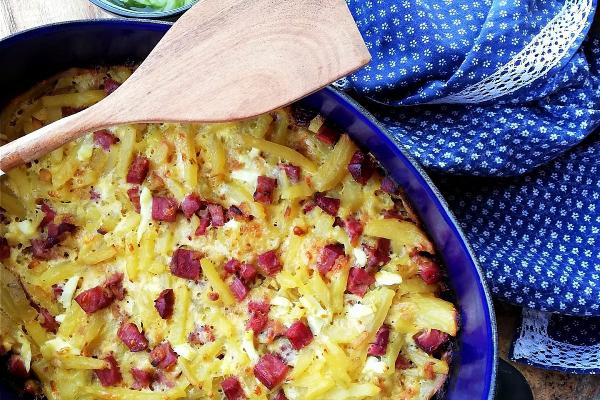 Potatoes baked with eggs, cheese and smoked meat served in a baking dish with a wooden spoon.