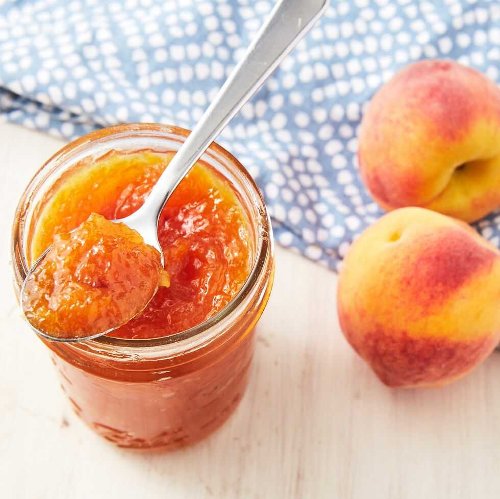 Pfirsich-Ingwer-Marmelade in einem Glas mit einem Löffel mit frischen Pfirsichen daneben.
