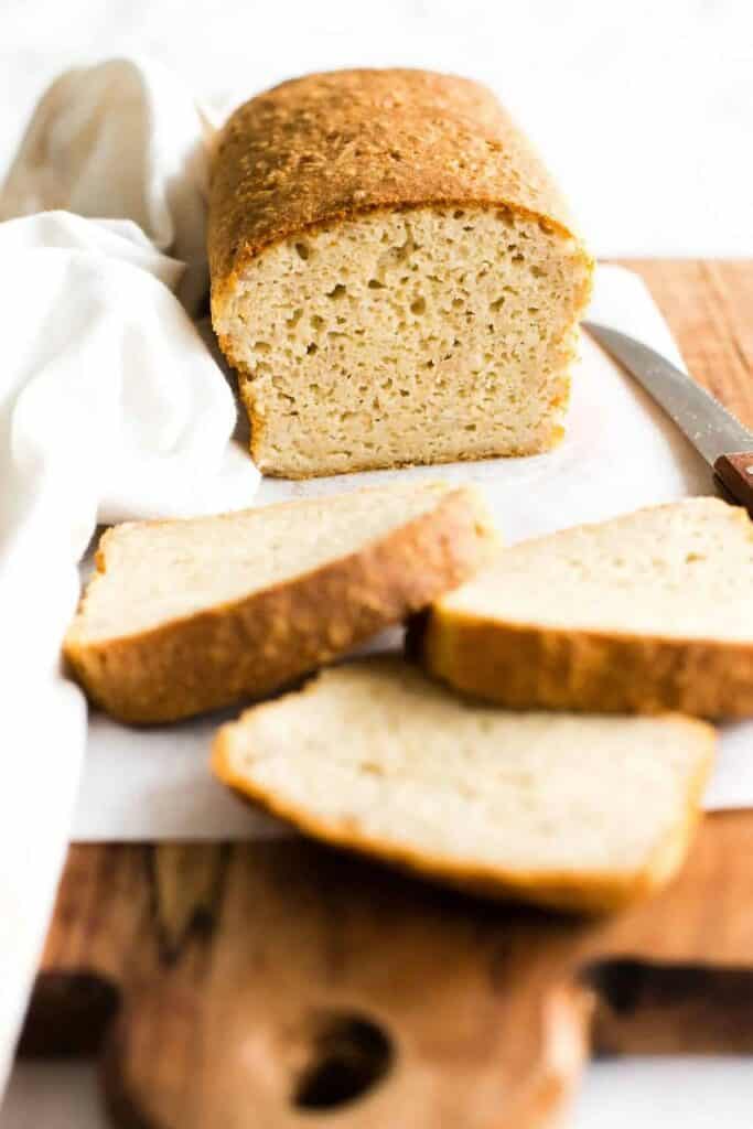 Nakrájený chléb bez lepku na utěrce, která je položena na dřevěném prkýnku.