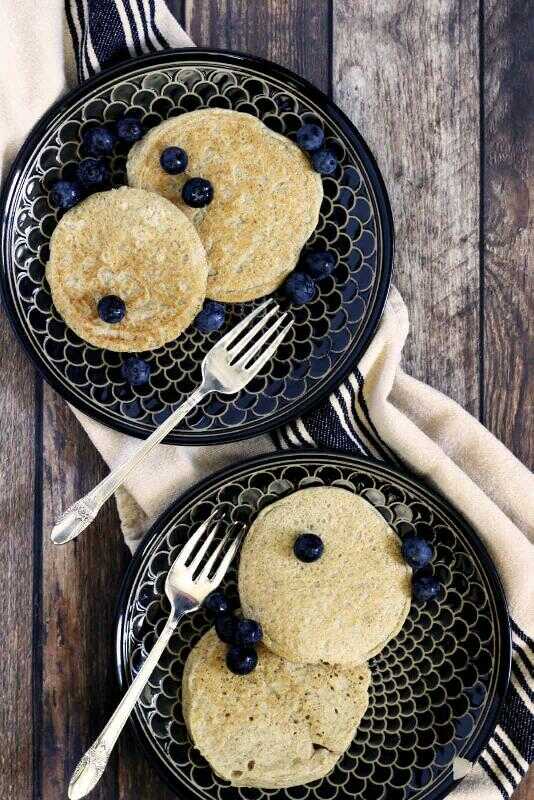 Gluten-free pancakes served on two plates with forks and decorated with fresh blueberries.