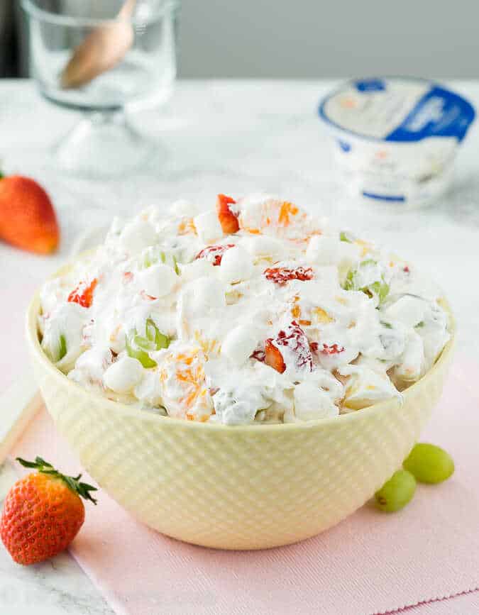 Salát ze svěžího ovoce a malých marsmallows v lehké a nadýchané směsi jogurtu a šlehačky servírovaný v misce.