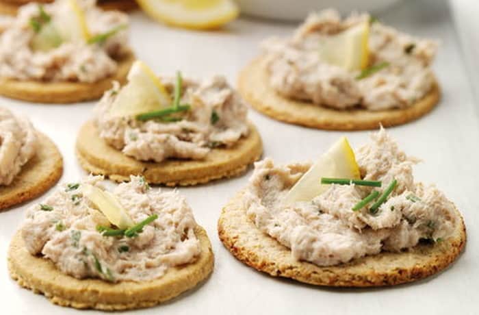 Smoked mackerel pâté on oat biscuits garnished with chives and lemon.