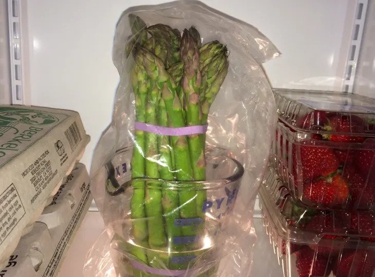 Grüner Spargel im Kühlschrank in einem Glas aufbewahrt und mit einer Plastiktüte abgedeckt.
