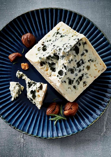 Lahodný francouzský sýr na modrém talířku s ořechy.