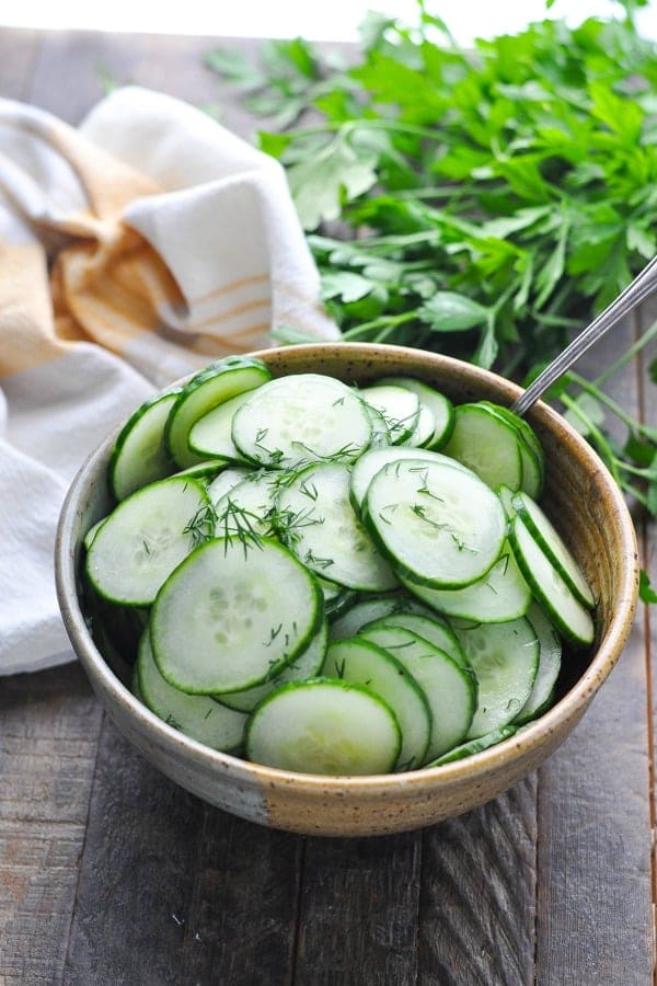 Slices of fresh cucumber sprinkled with dill in a bowl with a spoon.