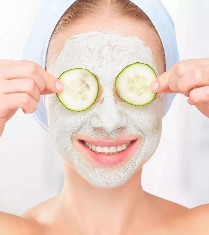 A woman wearing a facial mask and holding cucumber slices over her eyes.