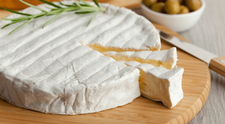 Nakrájený francouzský sýr na dřevěném prkénku.