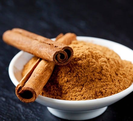 Ground cinnamon in a bowl together with sticks of cinnamon bark.