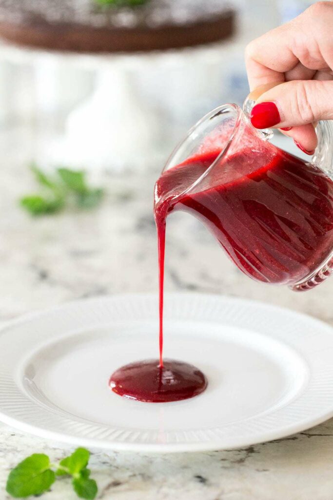 Raspberry dressing in a glass jug held by a hand and poured onto a plate.