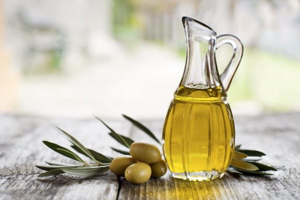 Olivenöl in einer Glasflasche und daneben platzierte grüne Oliven.