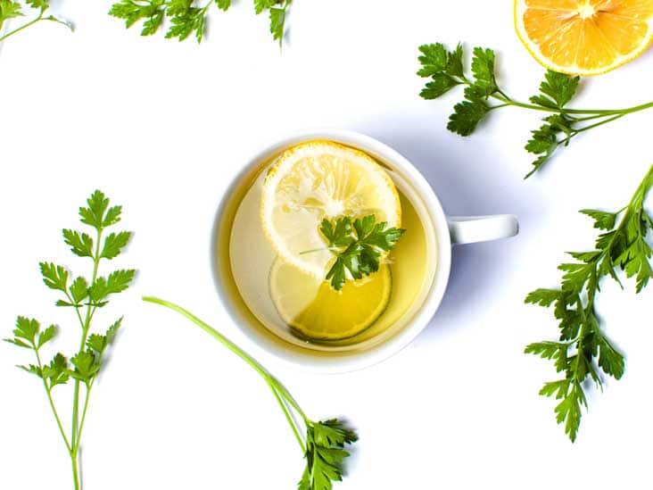 Parsley tea in a mug with lemon, with fresh parsley placed next to it.