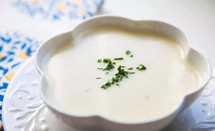 Francouzská polévka Vychyssoise servírovaná v mističce a ozdobená čerstvou bylinkou.