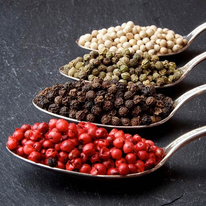Four spoons with four colored varieties of pepper originating from the black pepper tree.