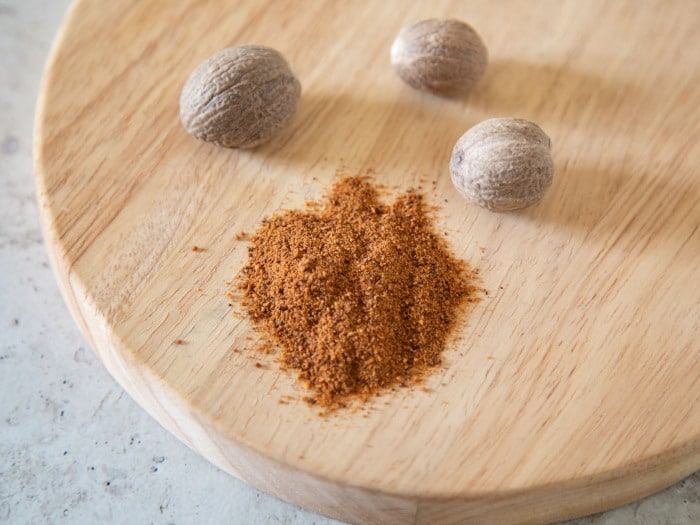Wooden cutting board with whole and ground nutmeg.