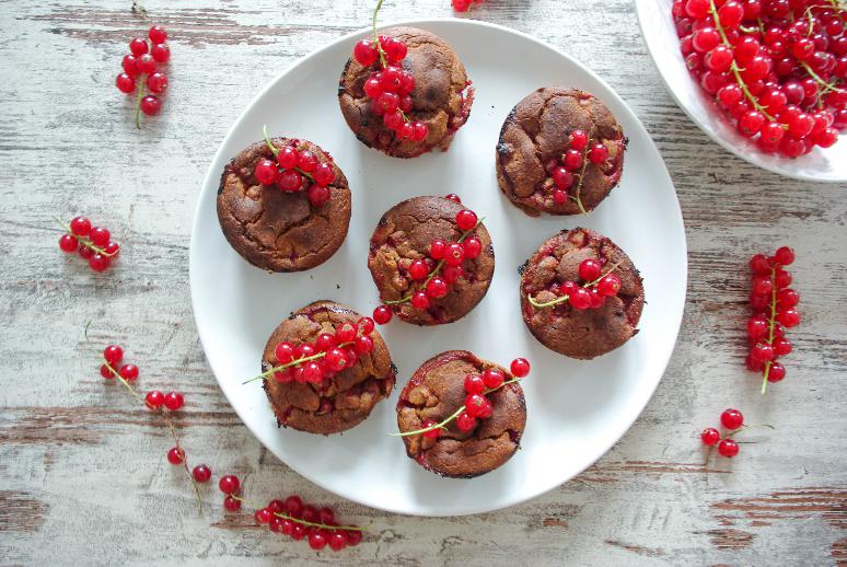 Muffins decorated with red currants served on a plate with fresh currants spread out next to it.