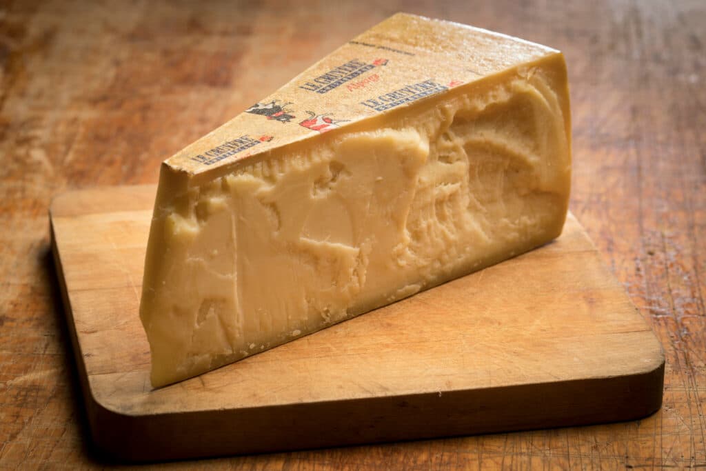 Klínek polotvrdého sýra na dřevěném prkénku.