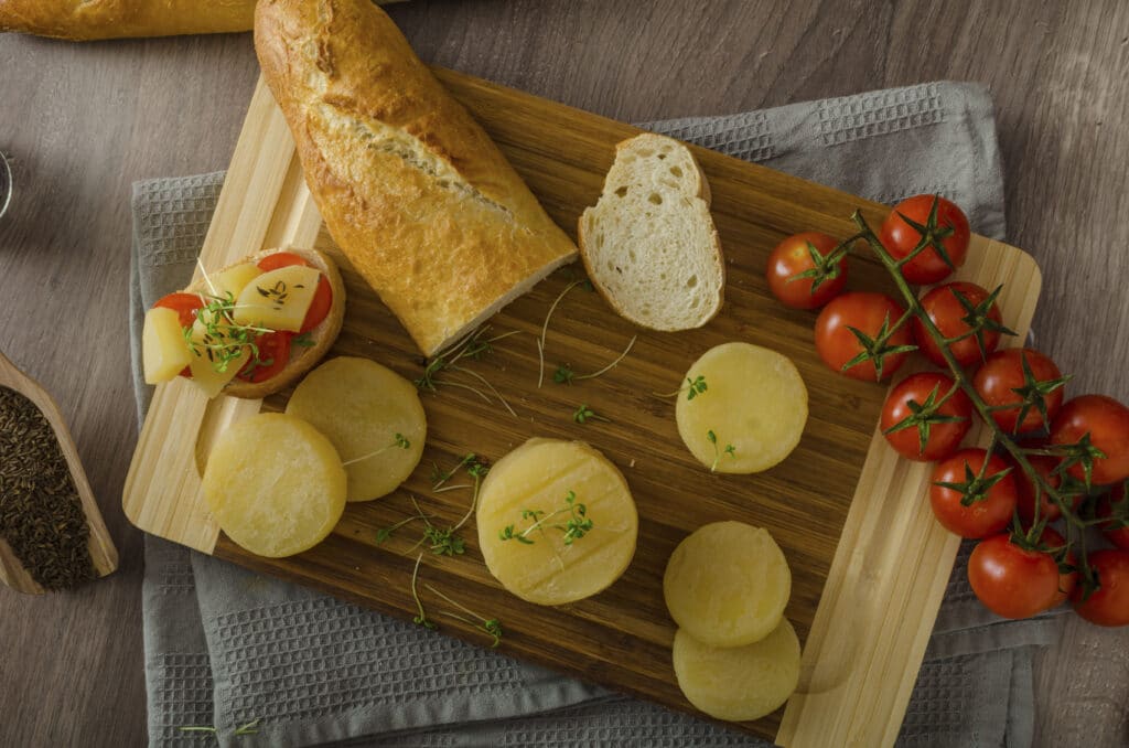 A wooden board on which rounds of cheese with tomatoes and a baguette are placed.