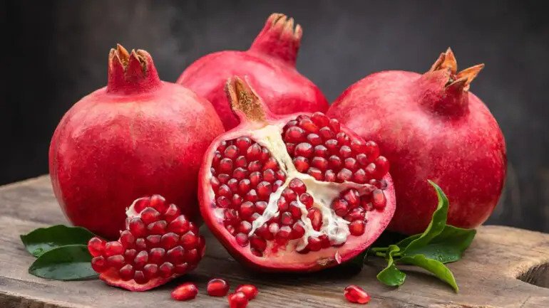 Whole fresh pomegranates and one halved on a cutting board.