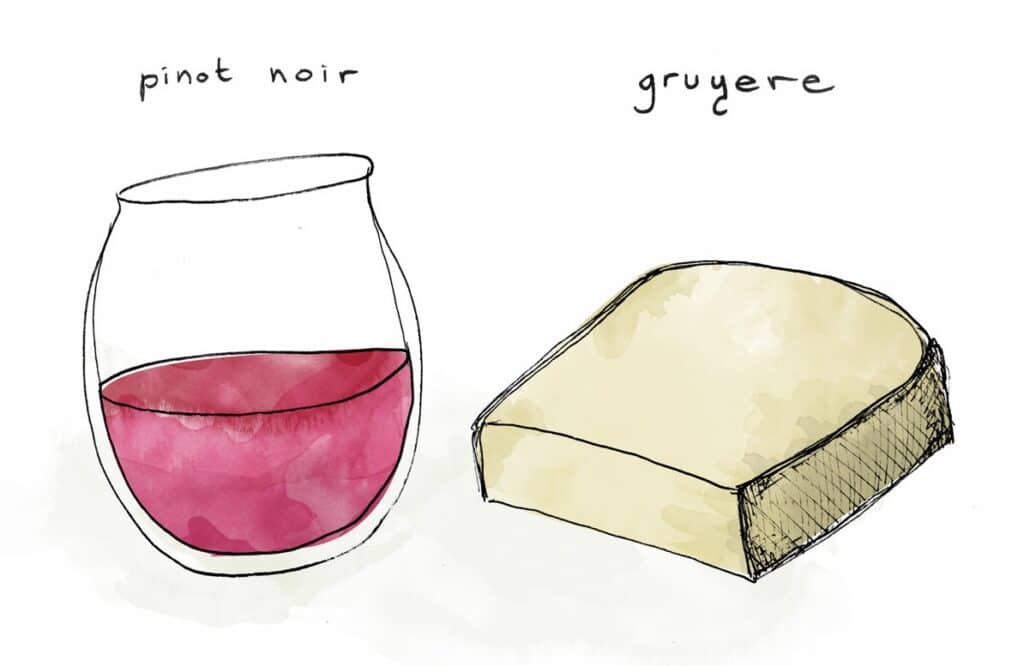 A painted glass of red wine along with a piece of cheese.