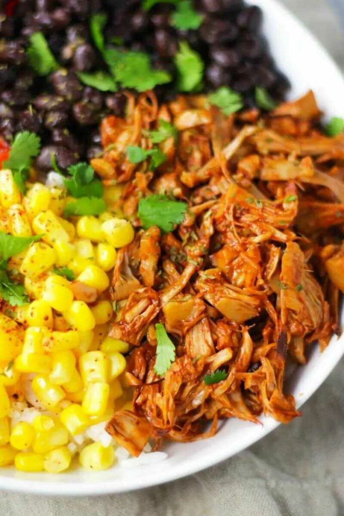 Shredded jackfruit served on a plate with corn, beans and fresh herbs.