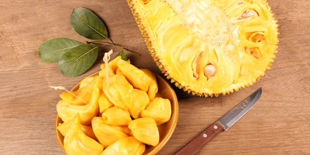 Rozkrojený jackfruit a mistička s nakrájeným jackfruitem s vedle položeným nožem.