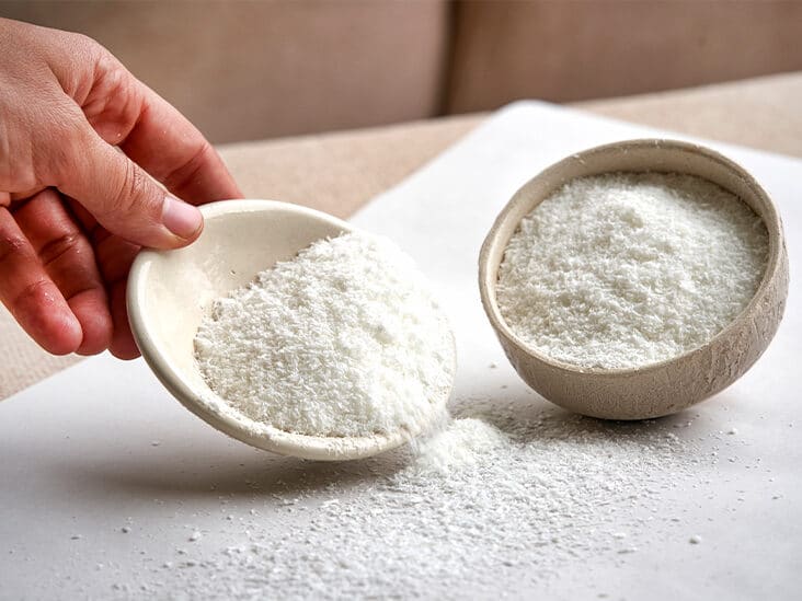 Coconut flour in a bowl and a hand holding a plate with flour, which she pours onto the table.