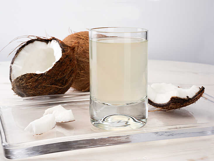 A glass of coconut water and fresh ripe coconuts placed next to it.