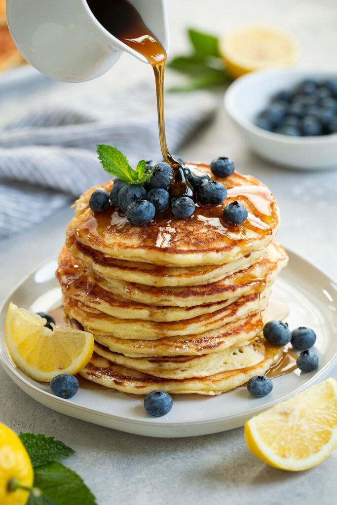 A mountain of pancakes with blueberries and drizzled with soft syrup.