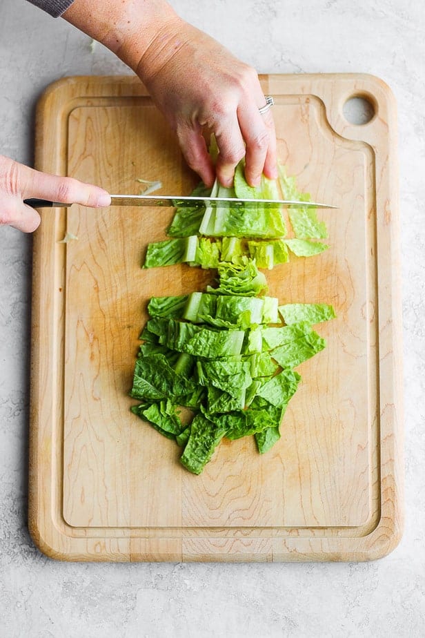 Hände schneiden einen Salat auf einem Schneidebrett mit einem Messer.