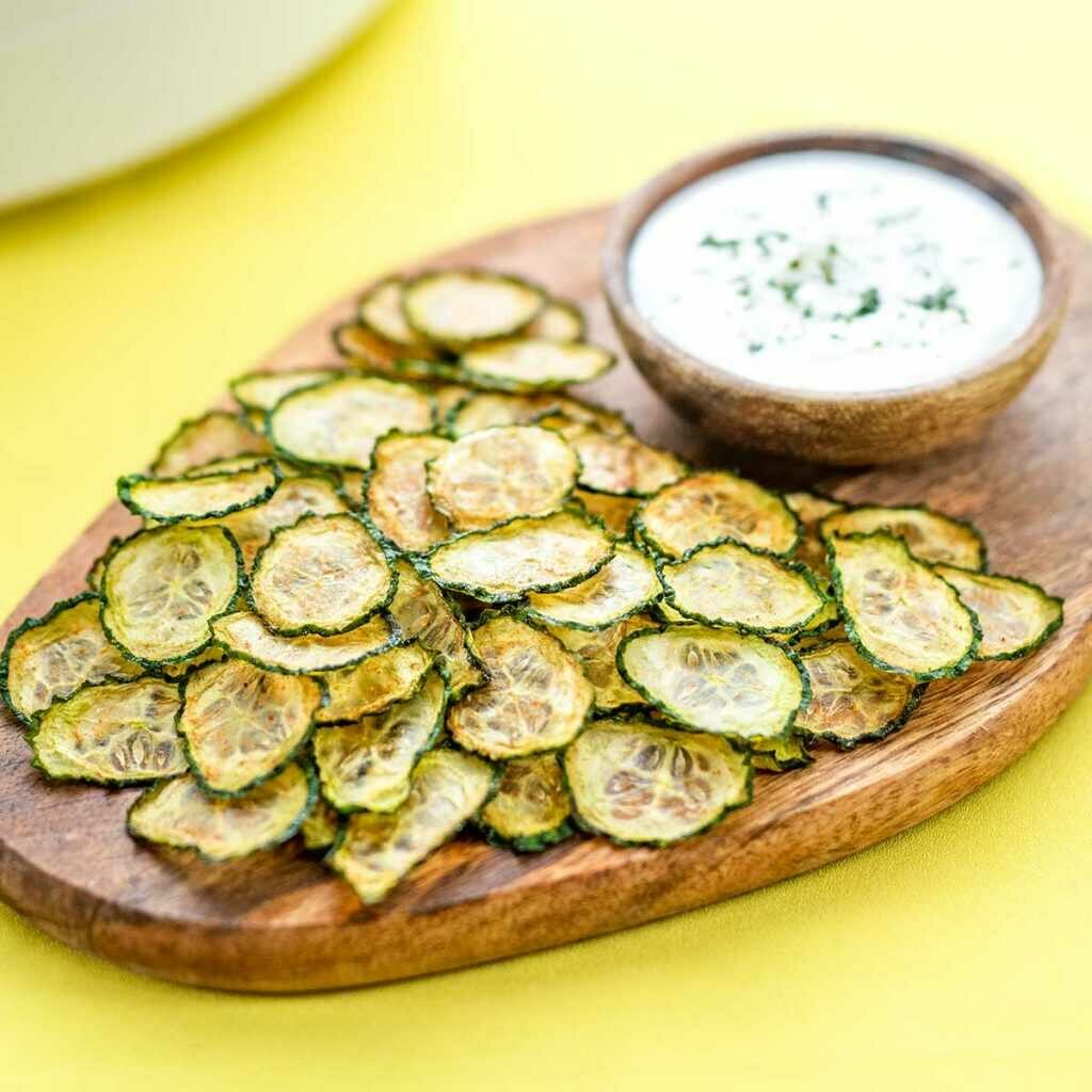 Cucumber chips on a cutting board with a bowl of dip.
