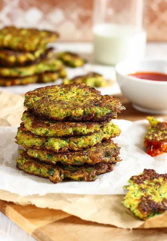 Broccoli and carrot pancakes stacked on top of each other and placed on a board covered with baking paper.